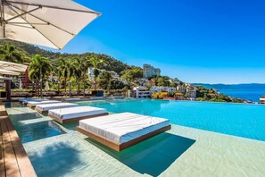 A poolside area with sunbeds and umbrellas, overlooking a coastal cityscape.