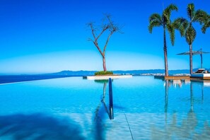 Una piscina infinita azul turquesa con vistas al océano y palmeras.