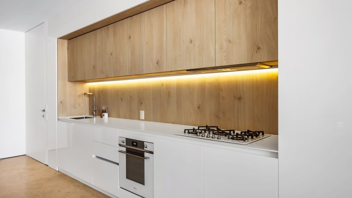 A modern kitchen with white cabinetry, a wooden upper section, a built-in oven, and a gas stove.
