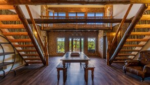 A spacious room with a high ceiling, a wooden table, and a view of the outdoors through large windows. - The Howling Buck Lodge (Logan)
