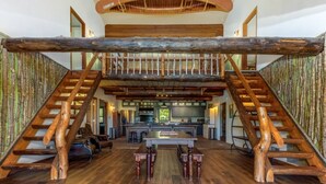 A spacious living area with a high ceiling, a central island, and a rustic staircase. - The Howling Buck Lodge (Logan)
