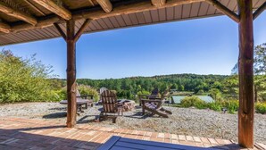 An outdoor seating area with Adirondack chairs and a wooden deck, overlooking a scenic landscape with trees and a lake. - The Howling Buck Lodge (Logan)