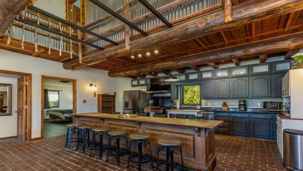A spacious kitchen with a large island, dark cabinets, and a rustic wooden ceiling. - The Howling Buck Lodge (Logan)
