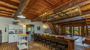 A rustic kitchen with a brick floor, wooden cabinets, and a dining area with a long table and chairs. - The Howling Buck Lodge (Logan)