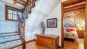 Un escalier avec des balustrades en bois menant à une chambre dotée d’un mur en pierre et d’un lit recouvert d’une couvre-lit à motifs floraux.