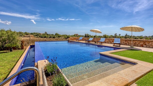 A clear blue pool with lounge chairs and umbrellas, surrounded by a stone wall and greenery. - Na Corme Nova by dracmallorca (Calonge)