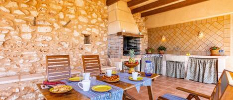 A rustic stone wall, wooden beams, a brick fireplace, and a tiled backsplash in a dining area.