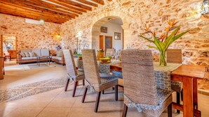 A rustic dining area with stone walls, wooden beams, wicker chairs, and a wooden table. - Na Corme Nova by dracmallorca (Calonge)