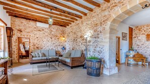 A rustic interior with exposed stone walls, wooden beams, a wicker sofa, and a large barrel. - Na Corme Nova by dracmallorca (Calonge)