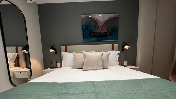 Ett modernt hotellrum med en stor säng, två sängbord, ett litet bord, ett konstverk som hänger på väggen och en spegel.