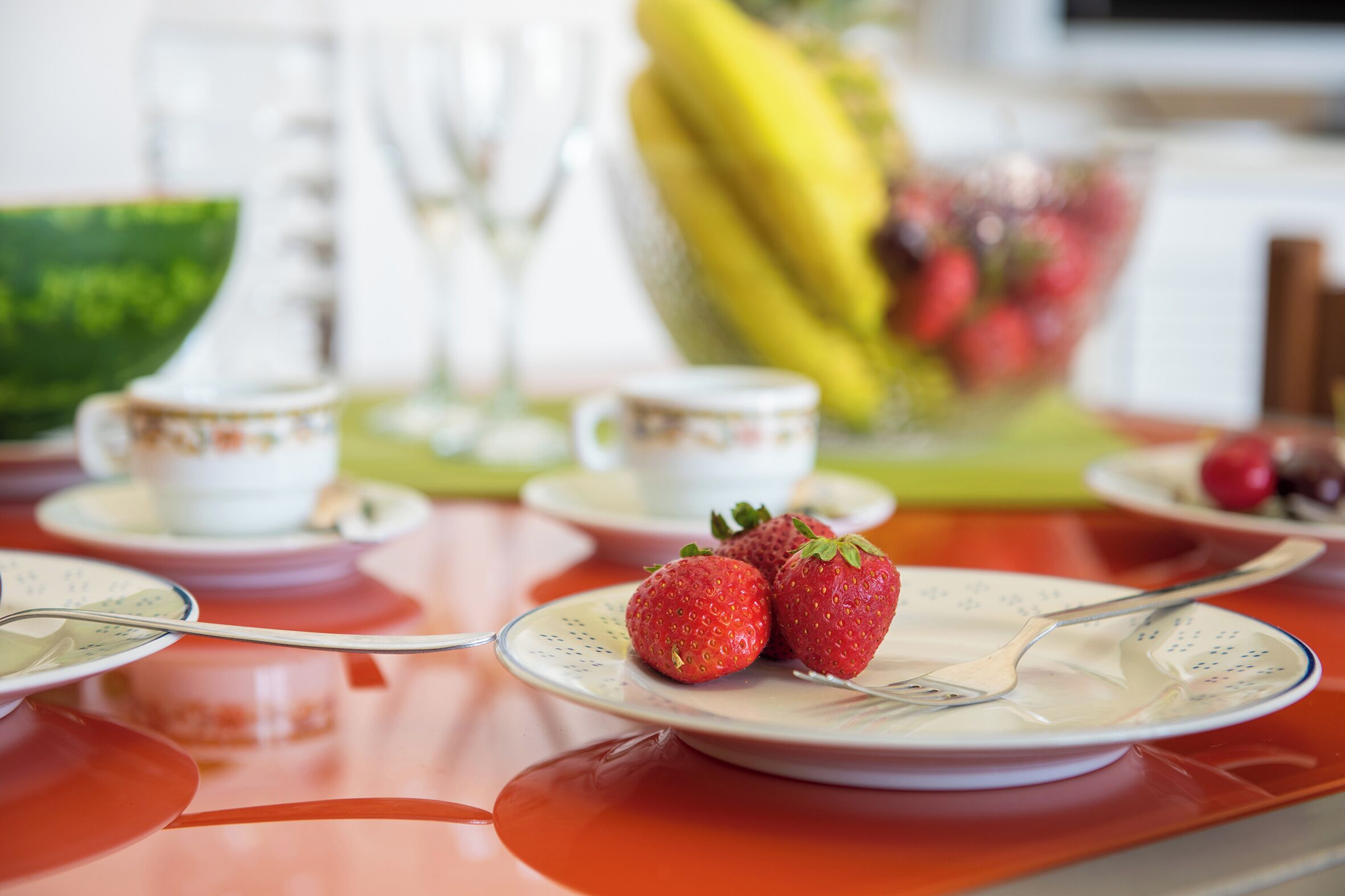 A table set with plates, cutlery, and a bowl of strawberries.