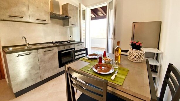 A modern kitchen with a stove, sink, and cabinets. There is a dining table with chairs and a vase of flowers. - Casa Ariel - Relaxation for couples near the beach (torre san giovanni)
