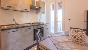 A modern kitchen with a gas stove, oven, and stainless steel sink. There is a sliding glass door leading to a balcony with a table and chairs. - Casa Ariel - Relaxation for couples near the beach (torre san giovanni)
