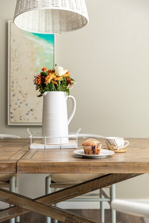 A wooden table with a white pitcher of flowers, a muffin, and a cup. - Pool & Play | Hot Tub, Ping Pong, Nintendo Switch (Stevensville)
