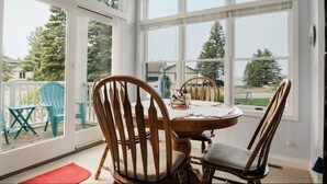 A dining area with a round table and four wooden chairs, large windows, and a view of the outdoors. - Main Floor, Easy Access Water View Condo (Manistee)