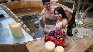 Ein hölzernes Whirlpool mit Kerzen, ein Holztisch mit Obstkorb, Weinflaschen und Gläsern.