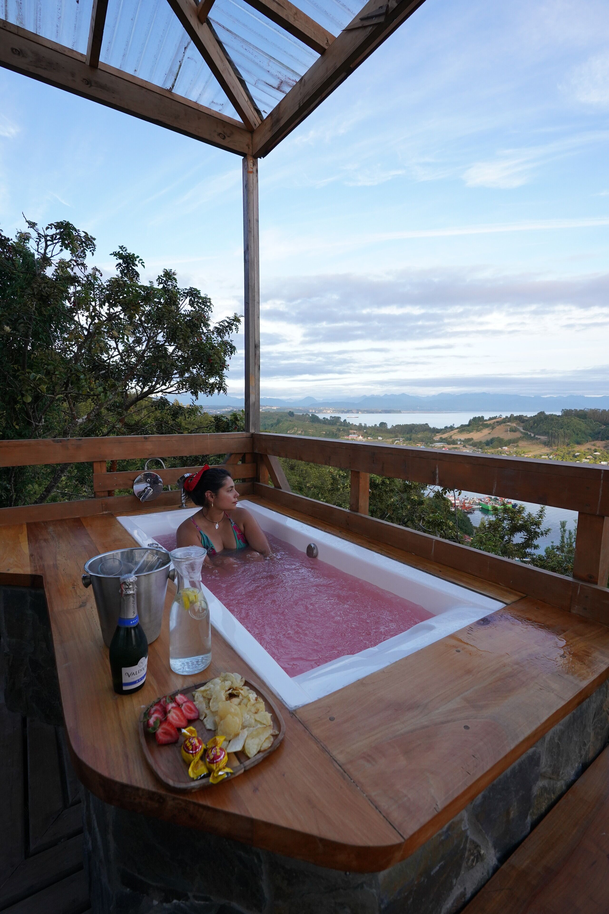 A wooden deck with a hot tub, a bottle of wine, and a tray of snacks.