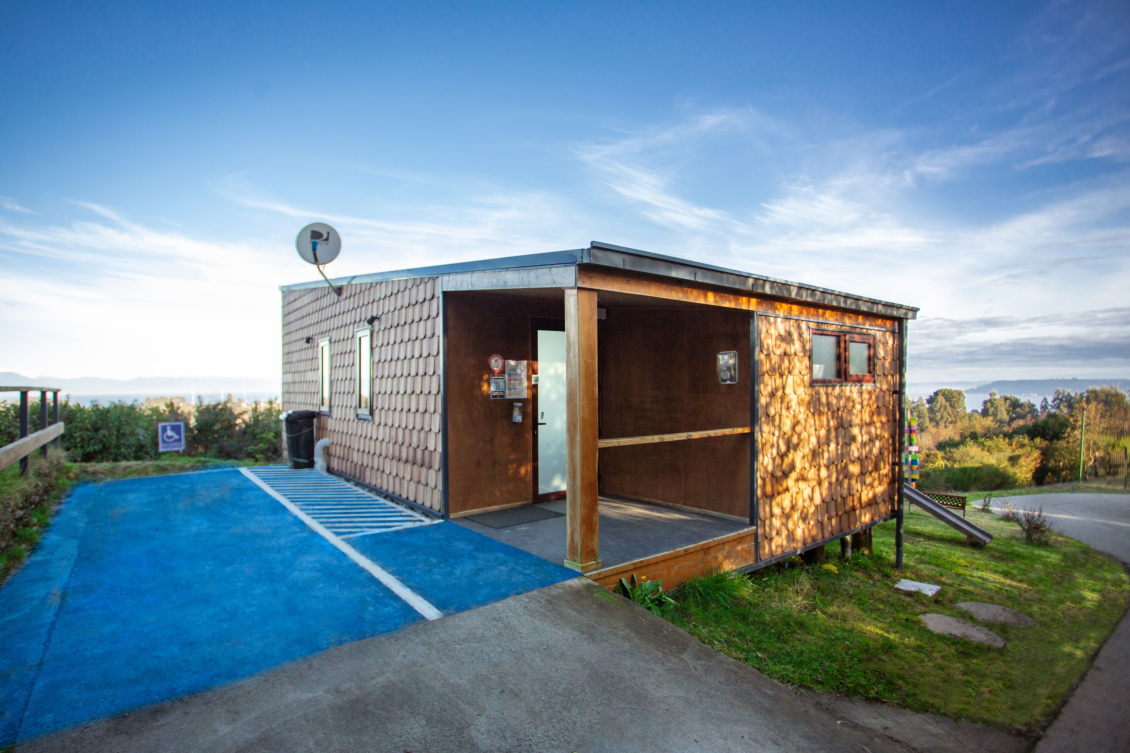 A small, modern building with a wooden exterior and a blue ramp leading to the entrance.