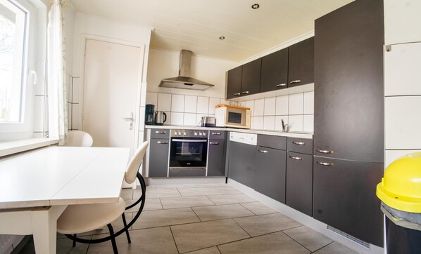 Compact kitchen with modern design, featuring a range hood, two ovens, microwave, and sink.