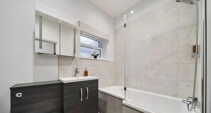 Ein modernes Badezimmer mit Dusche, Waschtisch inklusive Spiegel und einem Fenster über dem Waschbecken.