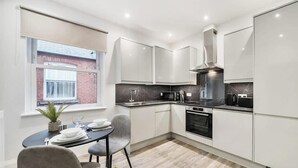 Een moderne keuken met witte kasten, een zwart aanrecht, een fornuis en een raam met uitzicht op een bakstenen gebouw.