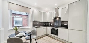 Une cuisine moderne avec des meubles blancs, un four encastré et un coin repas comprenant une table et des chaises.