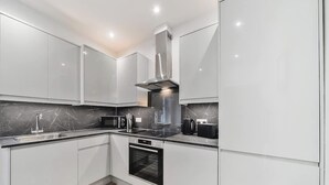 Een moderne keuken met witte kasten, een roestvrijstalen afzuigkap, een magnetron, een koffiezetapparaat en een oven.