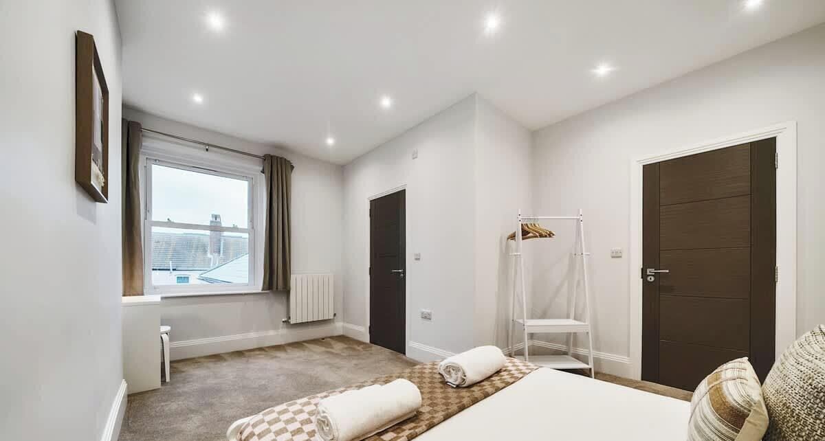 Ein Schlafzimmer mit großem Fenster, einem Bett, einem Sessel und einem Kleiderschrank.