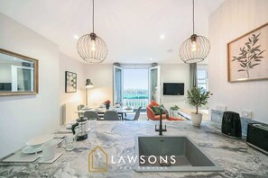 A modern kitchen with a marble countertop, two pendant lights, and a view to the outside. - Luxury 3BR Penthouse with Sea Views (Portsmouth)