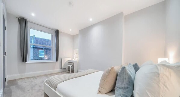 A bedroom with a bed, a desk, and a window with curtains. - Luxury 3BR Penthouse with Sea Views (Portsmouth)