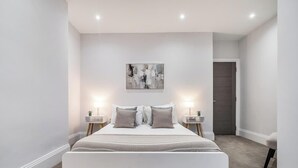 A bedroom with a large bed, two bedside tables, a wall-mounted artwork, and a door in the background. - Luxury 3BR Penthouse with Sea Views (Portsmouth)