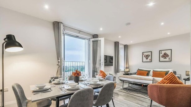 A modern living room with a dining area, a sofa, and a TV. - Luxury 3BR Penthouse with Sea Views (Portsmouth)