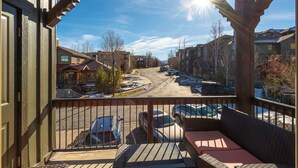 A balcony with a view of a residential street, wooden railings, and a clear sky.