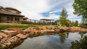 A residential area with a pond, large rocks, a pergola, and a house with a fenced yard.