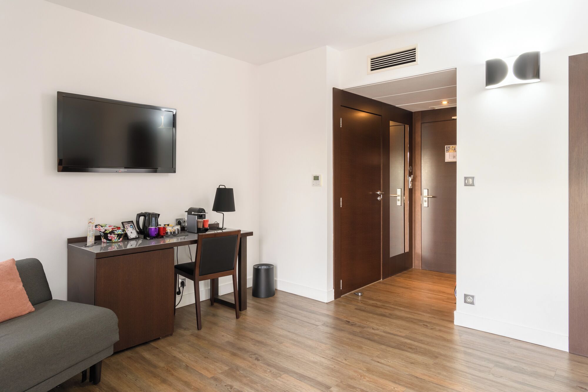 Une chambre d’hôtel moderne équipée d’une télévision à écran plat, d’un bureau avec une lampe, d’une chaise, d’un canapé et d’un plancher en bois.