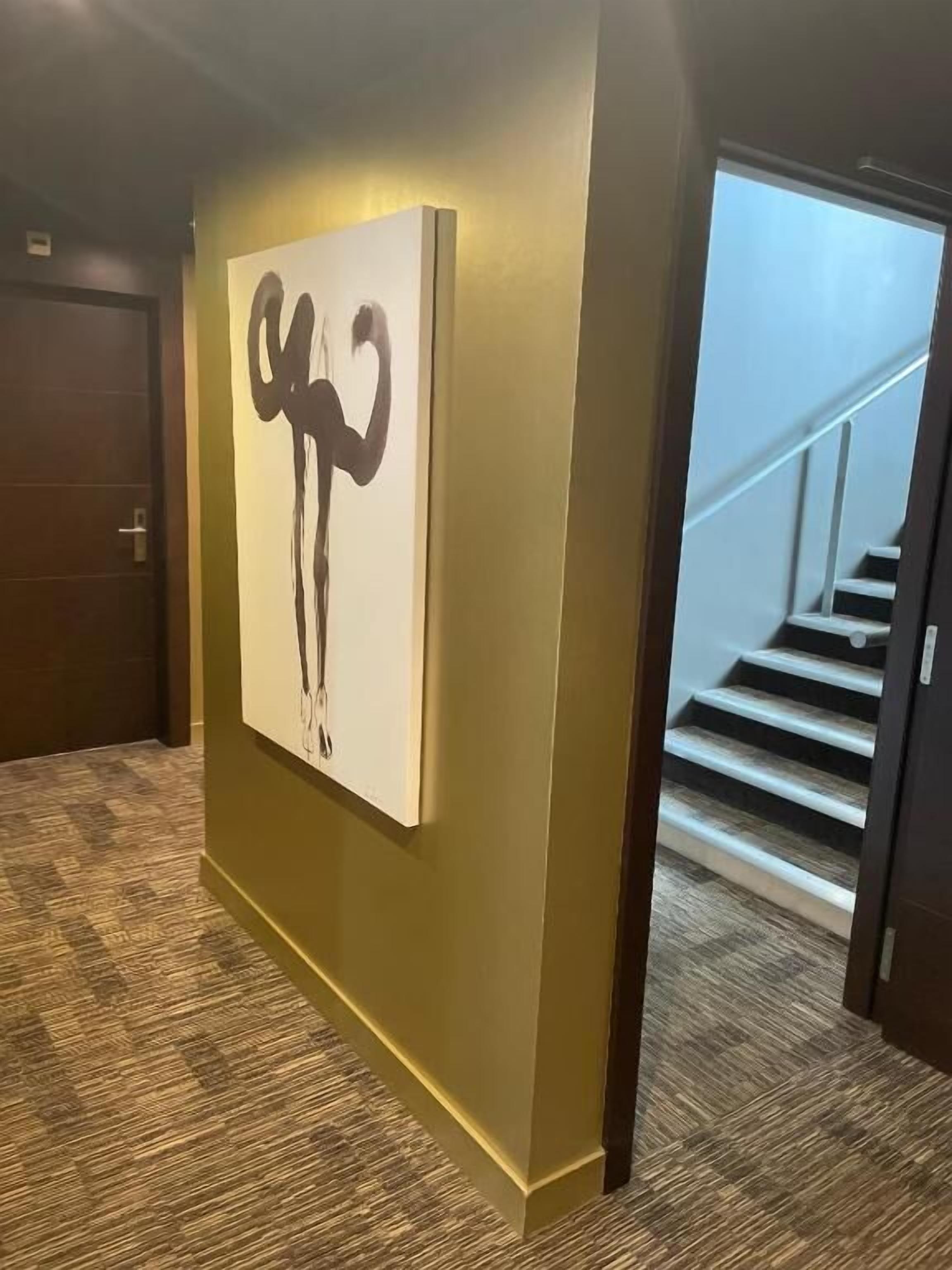 Un pasillo con un cuadro abstracto de gran tamaño en la pared, suelo cubierto de alfombra y una escalera al fondo.