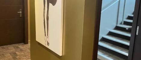 Un pasillo con un cuadro abstracto de gran tamaño en la pared, suelo cubierto de alfombra y una escalera al fondo.