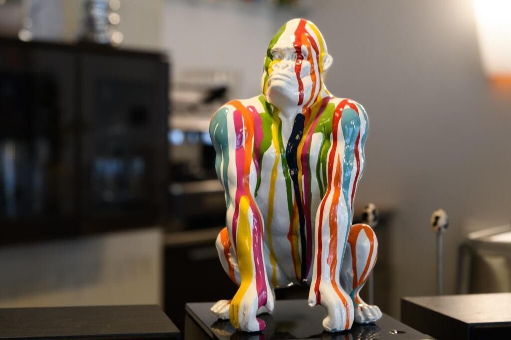A colorful sculpture of a human figure on a black pedestal in a room with a blurred background.