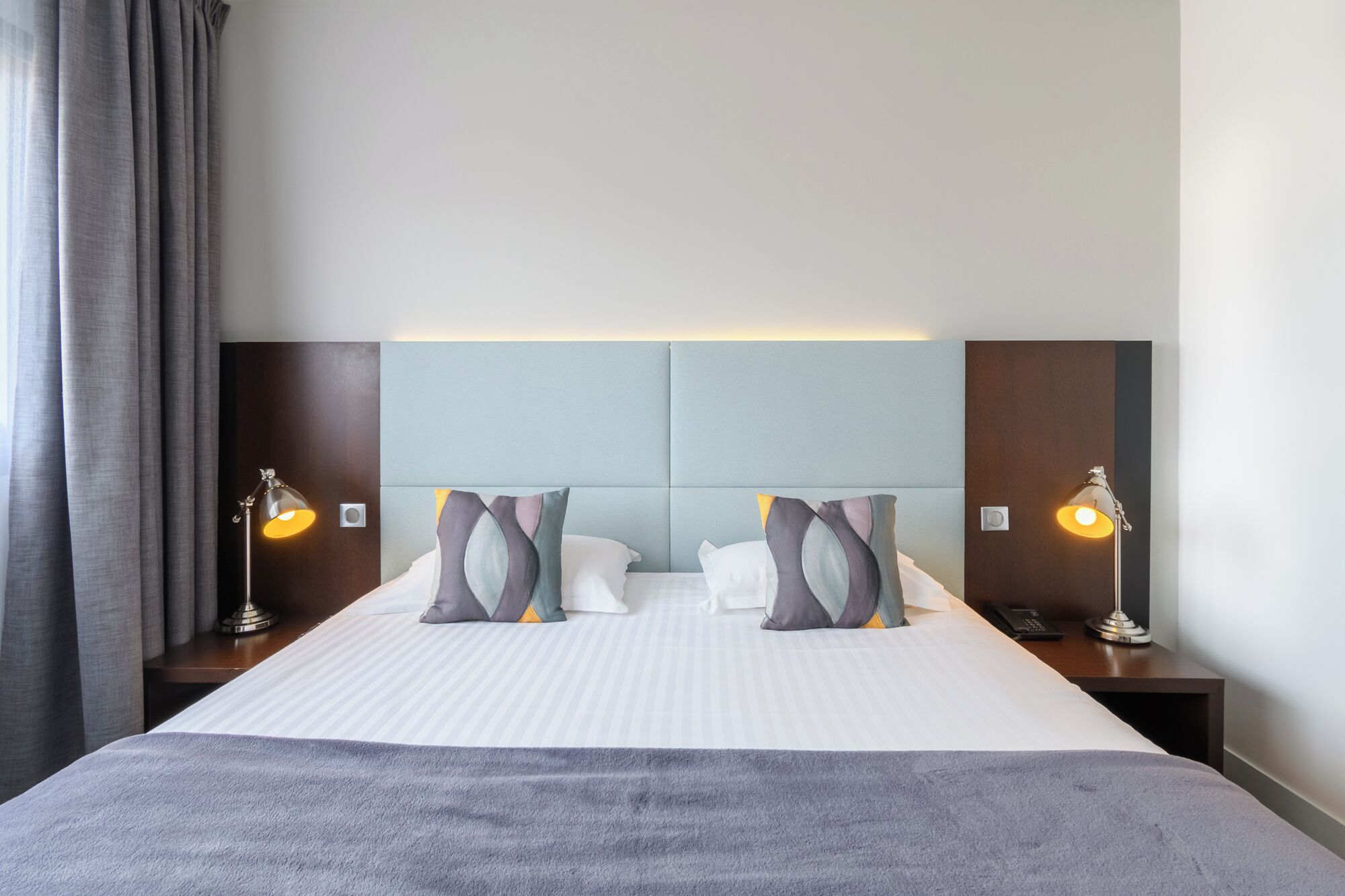 A hotel room with a large bed, two bedside lamps, and a headboard with a light panel.