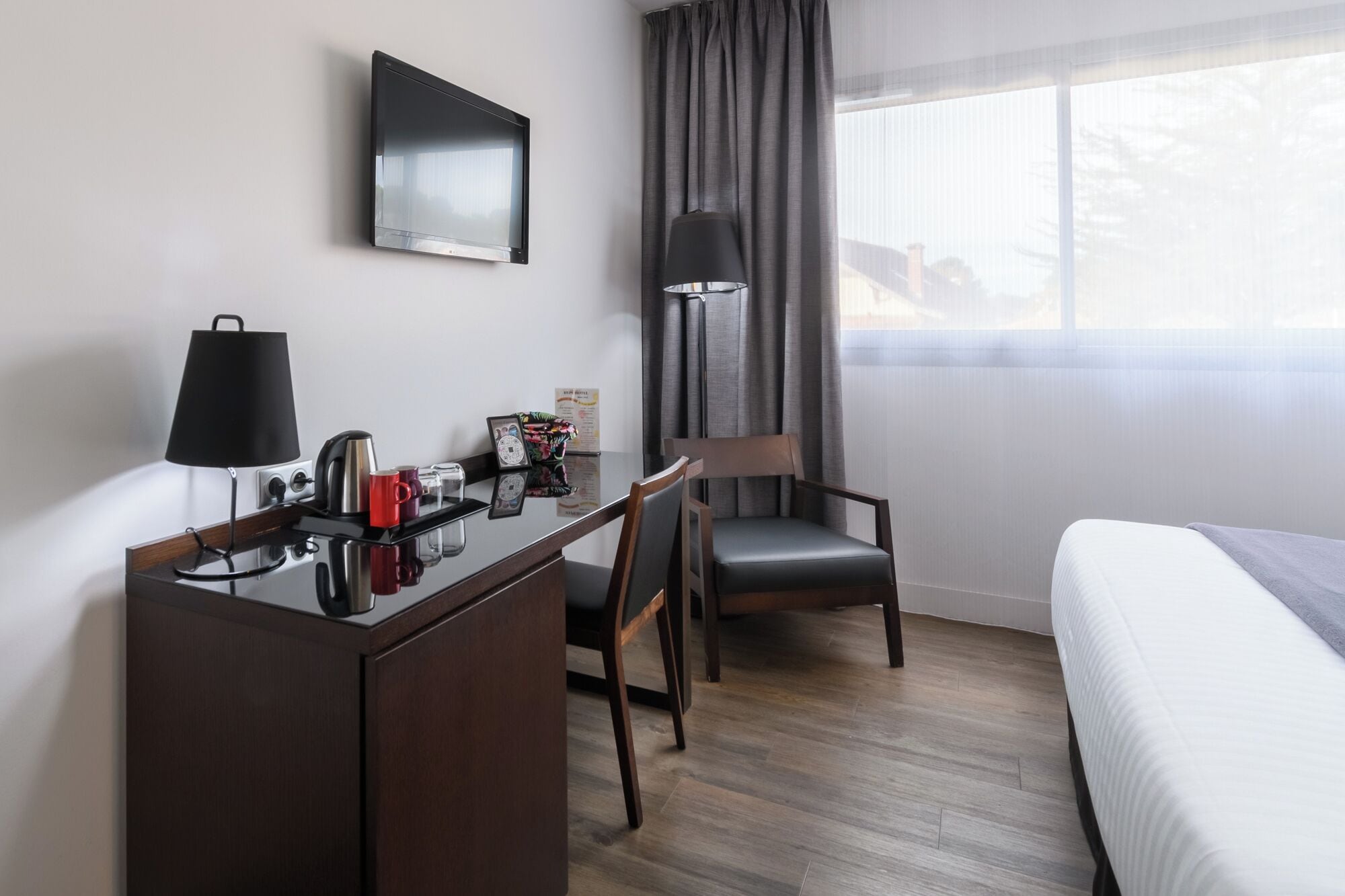 Een hotelkamer met een bureau, stoel, bed en een raam met gordijnen.