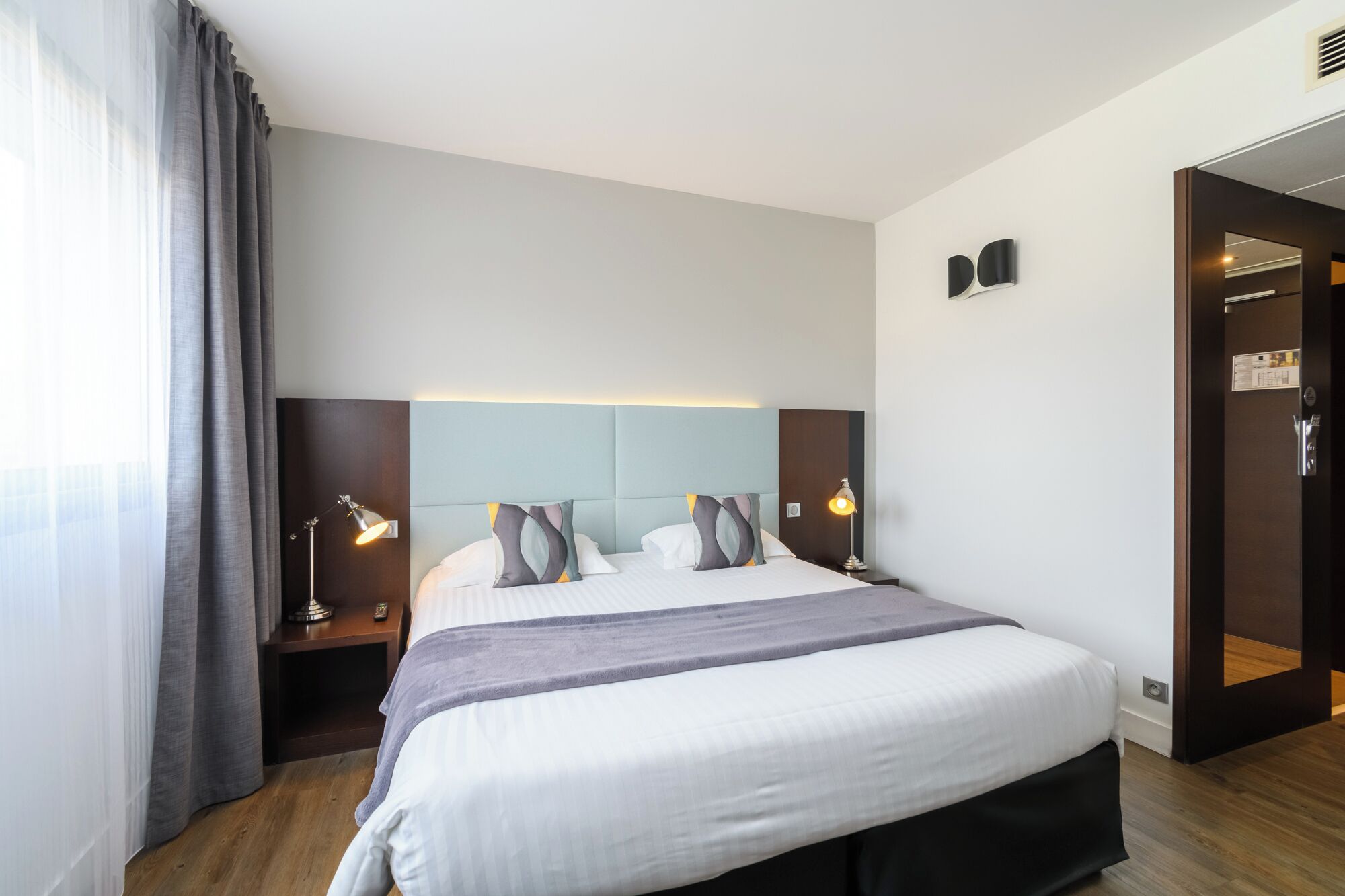 A modern hotel room with a large bed, two bedside tables with lamps, a headboard, and a wardrobe.