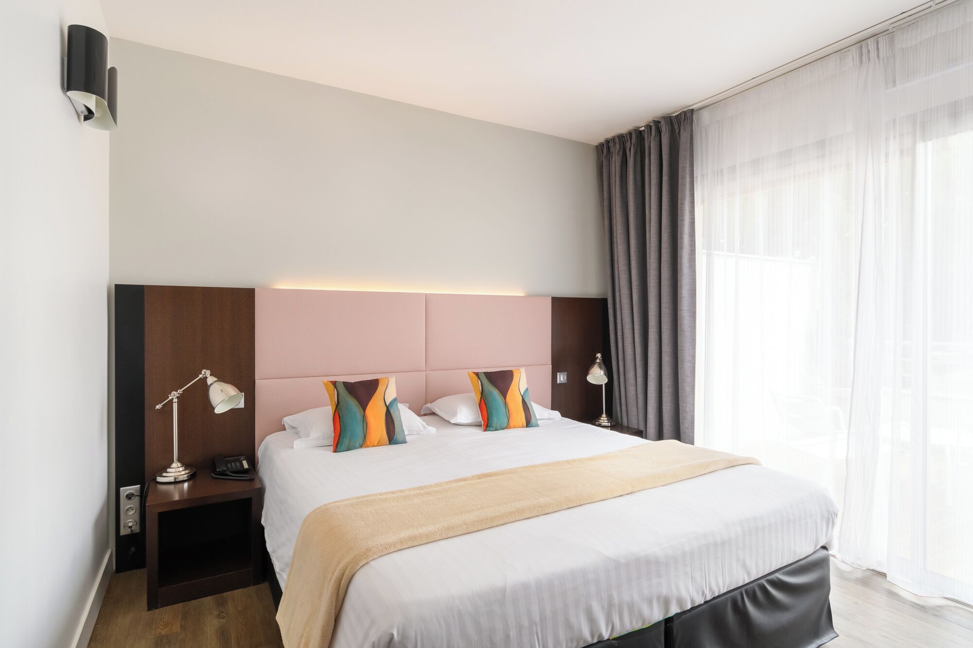 A modern hotel room with a large bed, a bedside table with a lamp, and a headboard with built-in lighting.