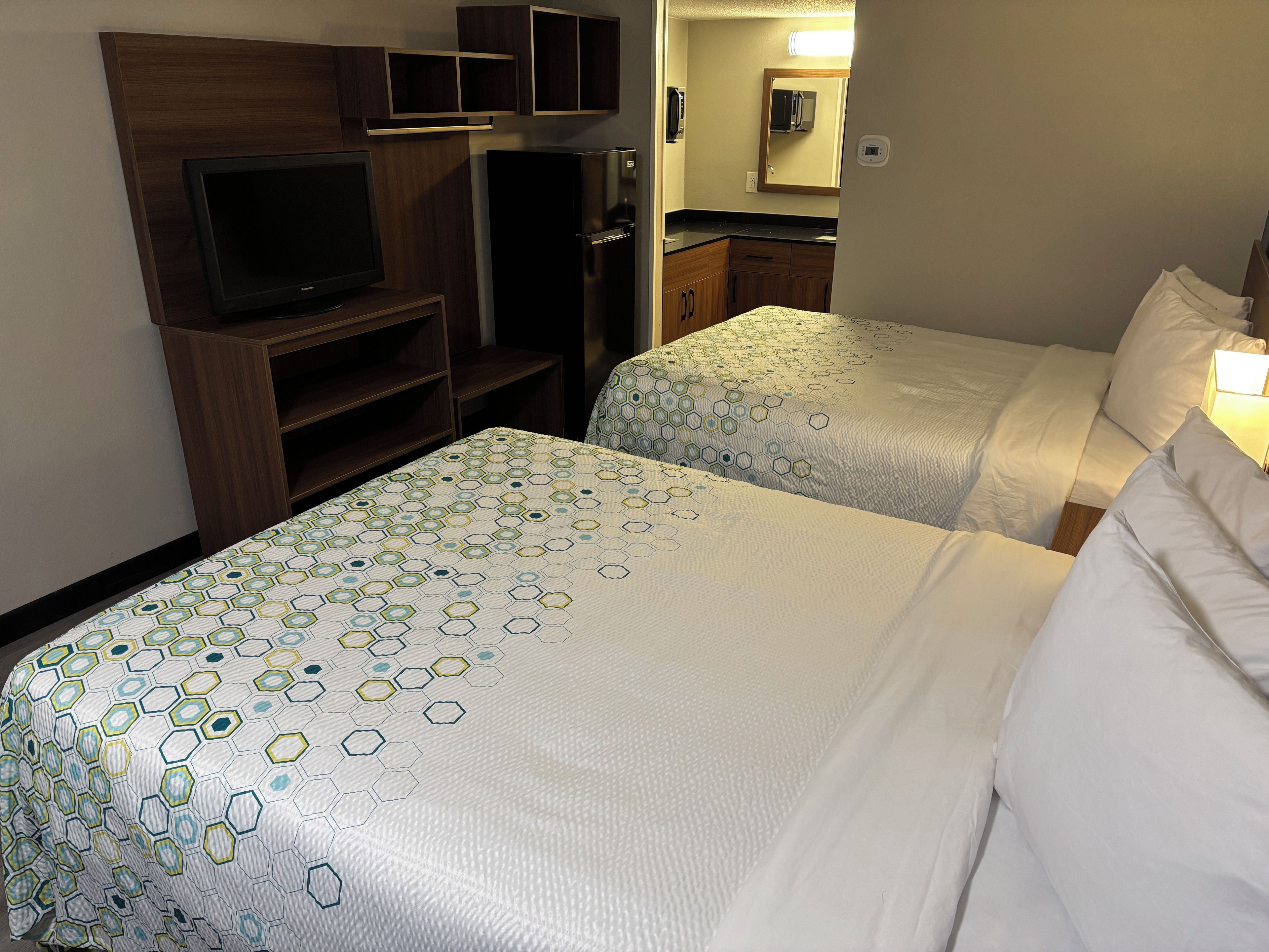 A hotel room with two beds, a TV, a refrigerator, and a microwave.
