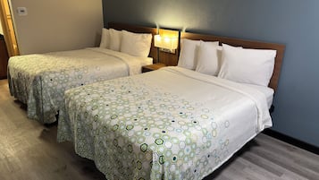 A hotel room with two beds, each with a patterned bedspread, a nightstand with a lamp, and a wall-mounted thermostat.