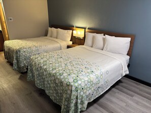Une chambre d’hôtel avec deux lits, chacun recouvert d’une couvre-lit à motifs, une table de chevet avec une lampe et un thermostat fixé au mur.