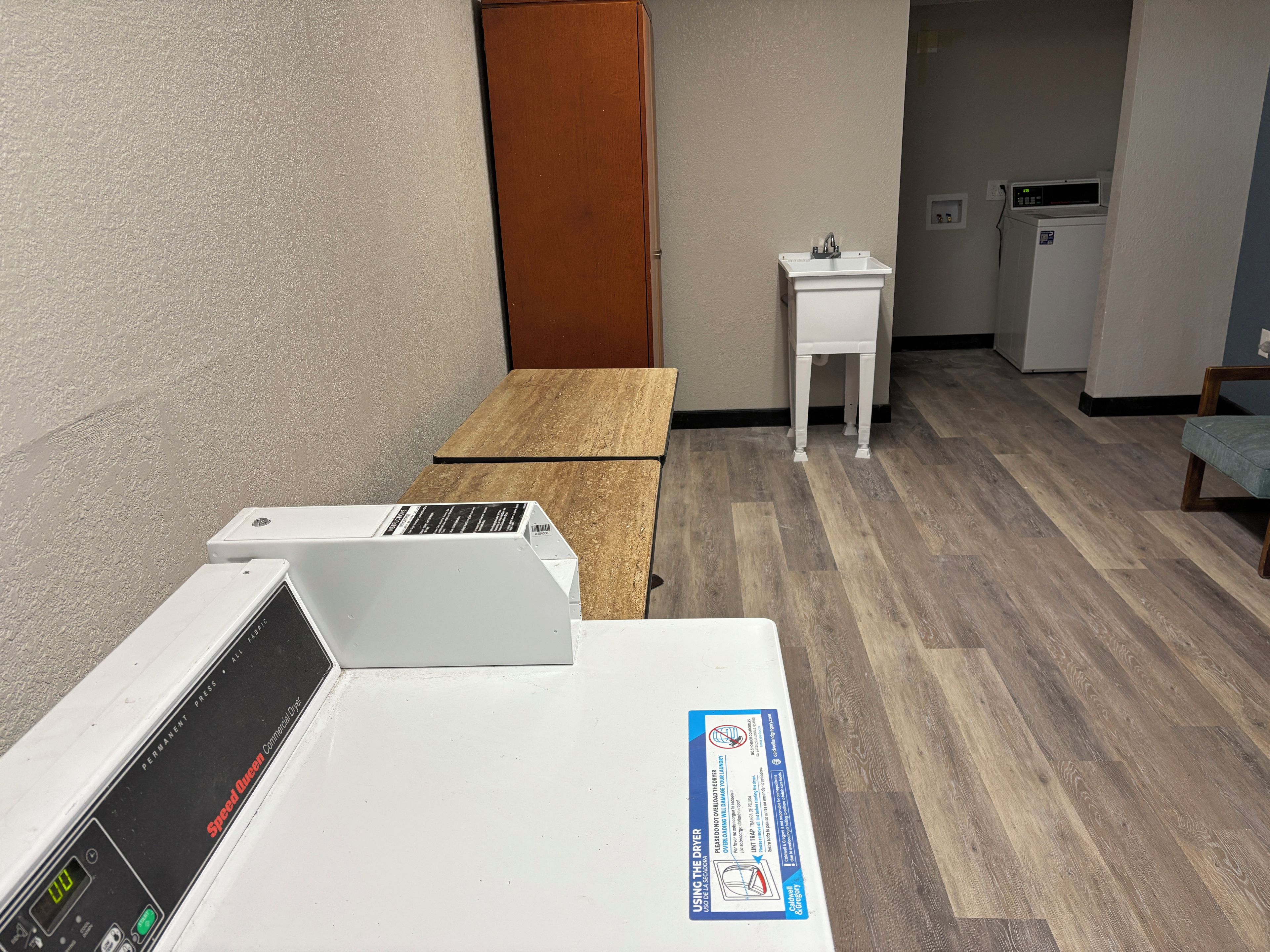 Une pièce avec une table en bois, un sèche-linge blanc, un petit évier et un four à micro-ondes.