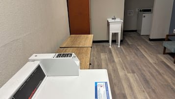 Una habitación con una mesa de madera, un secadora blanco, un lavamanos pequeño y un microondas.