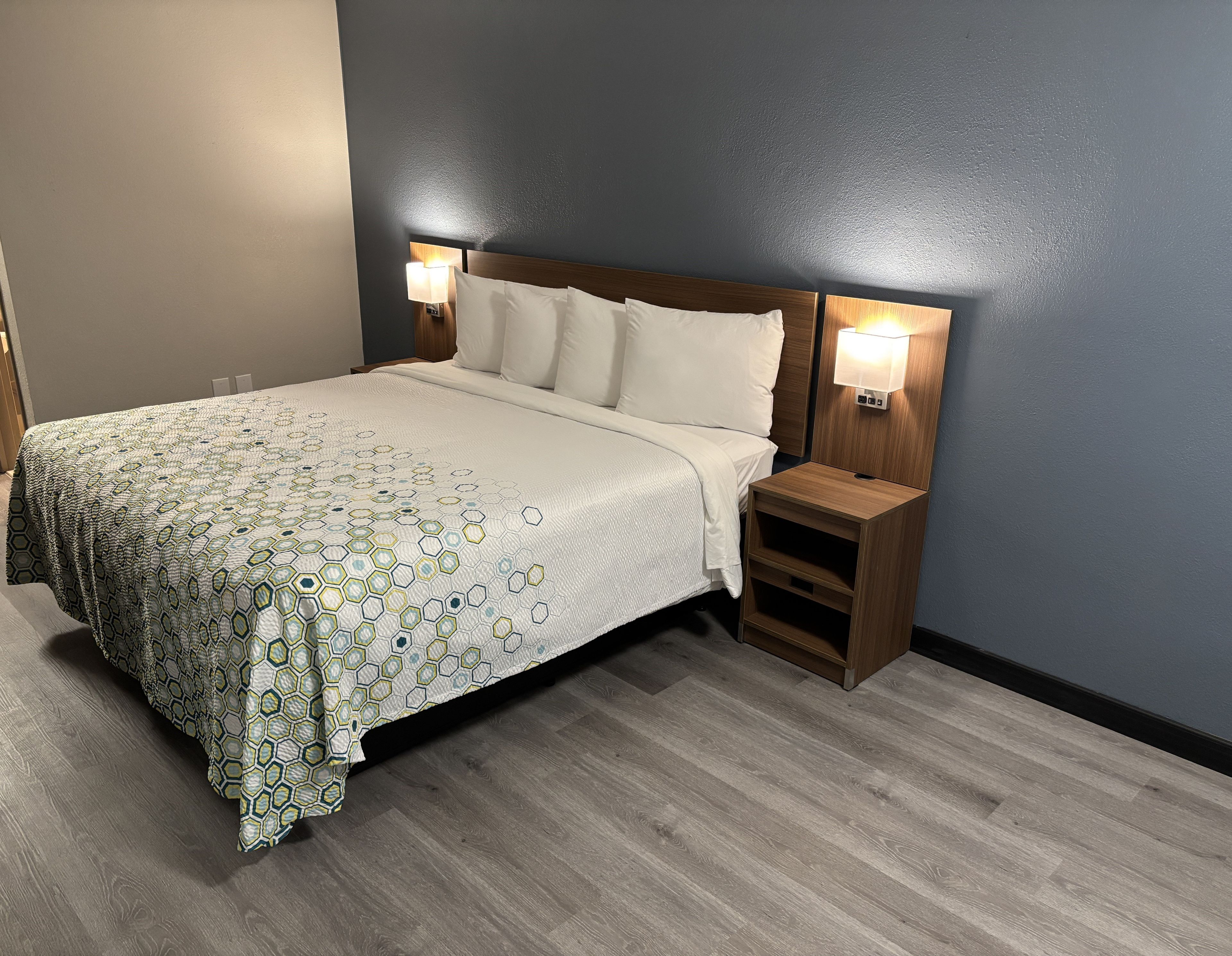 A neatly made bed with a patterned bedspread, two bedside lamps, and a wooden nightstand with a shelf.