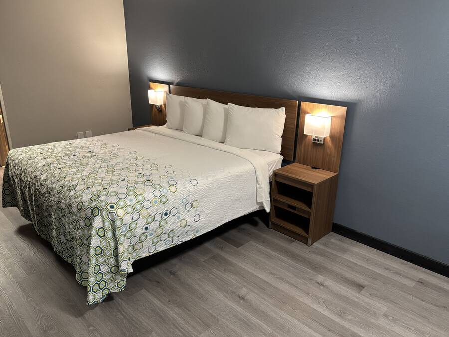 Una cama bien hecha con una colcha estampada, dos lámparas de noche y una mesita de noche de madera con un estante.