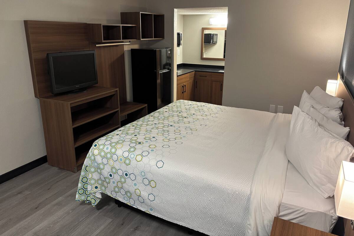 Habitación de hotel con cama, televisión, armario y baño visible a través de una puerta abierta.